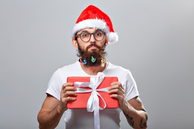 Weihnachten, Feiertage, Friseursalon und Stilkonzept - junger gutaussehender bärtiger Weihnachtsmann mit vielen kleinen Weihnachtskugeln im langen Bart.