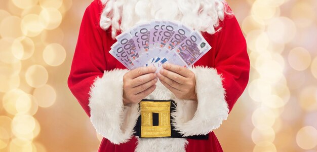 weihnachten, feiertage, gewinnen, währung und personenkonzept - nahaufnahme des weihnachtsmannes mit eurogeld über beigem lichthintergrund