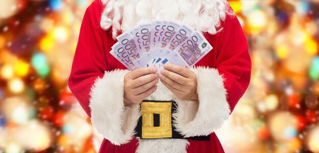 weihnachten, feiertage, gewinnen, währung und personenkonzept - nahaufnahme des weihnachtsmannes mit eurogeld über rotem lichthintergrund