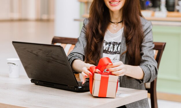 Weihnachten, Feiertage, Technologie und Einkaufskonzept - lächelnde Frau mit Kreditkarte auf dem Tisch, Geschenkbox und Laptop-Computer. Horizontales Foto