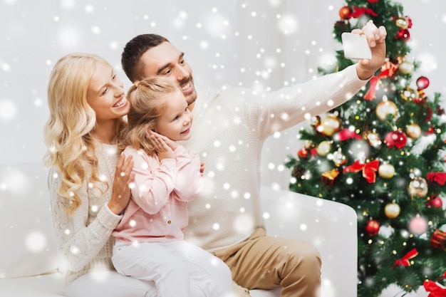 weihnachten, feiertage, technologie und personenkonzept - glückliche familie, die auf dem sofa sitzt und zu hause ein selfie-foto mit dem smartphone macht