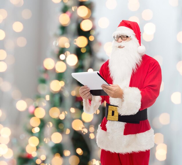 weihnachten, feiertage und menschenkonzept - mann im weihnachtsmannkostüm mit notizblock über baumlichthintergrund