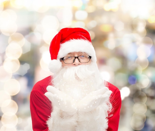 weihnachten, feiertage und personenkonzept - mann im kostüm des weihnachtsmannes, der auf palmen über lichthintergrund bläst