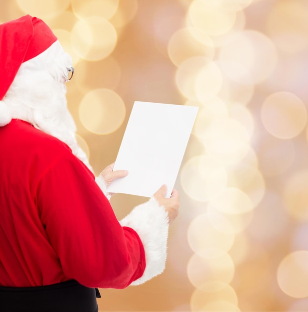 weihnachten, feiertage und personenkonzept - mann im kostüm des weihnachtsmannes, der brief über beigem lichthintergrund liest