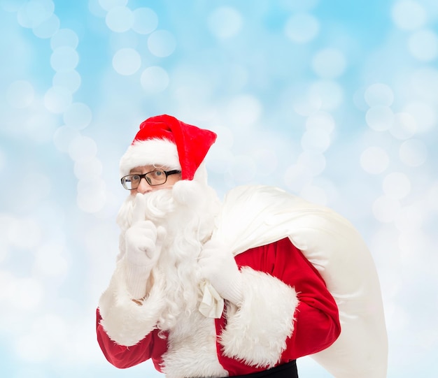 weihnachten, feiertage und personenkonzept - mann im kostüm des weihnachtsmannes mit tasche, die stille geste über blauem lichthintergrund macht