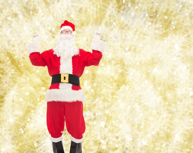weihnachten, feiertage und personenkonzept - mann im kostüm des weihnachtsmanns, der spaß über gelbem lichthintergrund hat