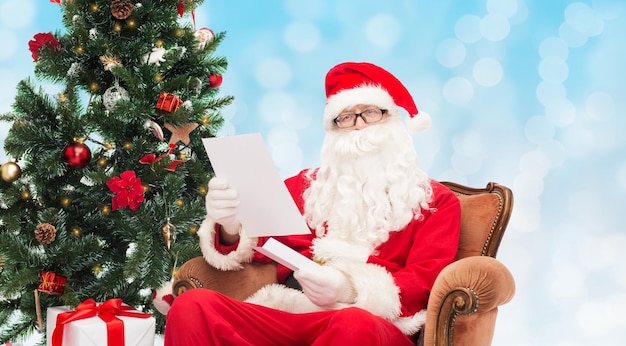 weihnachten, feiertage und personenkonzept - mann im kostüm des weihnachtsmanns mit brief über blaulichthintergrund