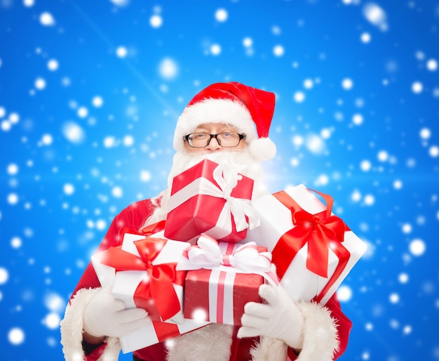 weihnachten, feiertage und personenkonzept - mann im kostüm des weihnachtsmanns mit geschenkboxen über blauem schneebedecktem hintergrund