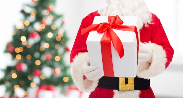 weihnachten, feiertage und personenkonzept - nahaufnahme des weihnachtsmanns mit geschenkbox über wohnzimmer mit baum