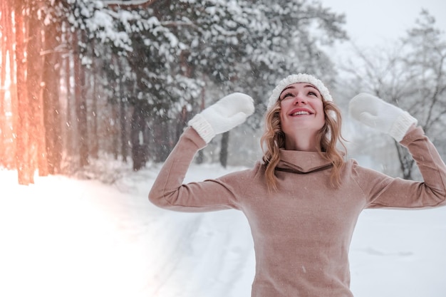 Weihnachten, Feiertage und Saisonkonzept. Junge glückliche Frau, die Schnee in der Winterwaldnatur durchbrennt. Warme Kleidung Strickhandschuhe und Mütze. Hintergrund der Winterwaldlandschaft