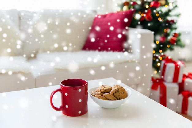 weihnachten, feiertage, winter, feier und stilllebenkonzept - nahaufnahme von haferkeksen und roter tasse auf dem tisch zu hause