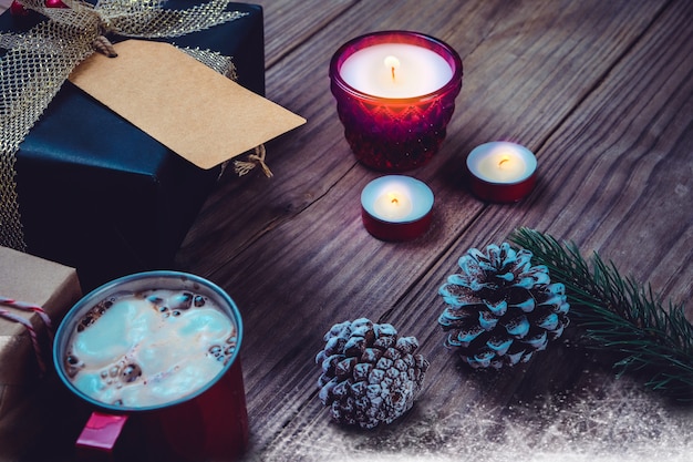 Weihnachten Hintergrund mit handgefertigten Geschenk Geschenk-Boxen und rustikale Dekoration mit Kerze, heiße Schokolade auf Holz Tisch in Weihnachten Nacht Party. Vintage Farbe Stil.