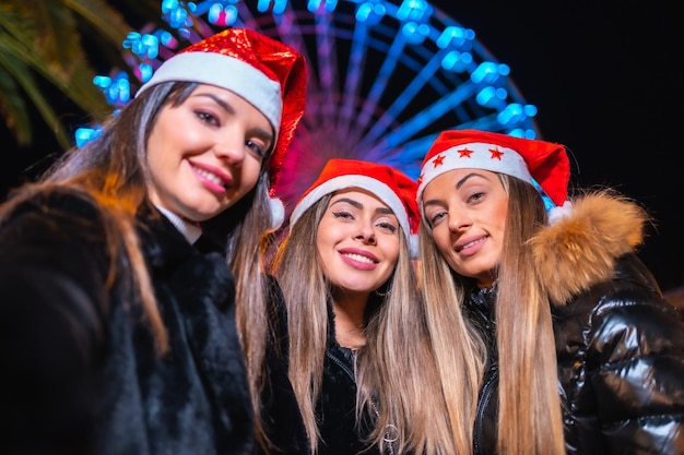 Weihnachten in der Stadt bei Nachtdekoration im Winter Freunde auf einem beleuchteten Riesenrad machen ein Selfie