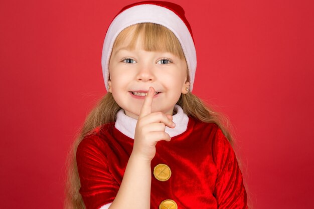Weihnachten ist nahe! Nahaufnahmeporträt eines kleinen niedlichen Mädchens im Weihnachtsoutfit, das stilles Gestik auf Rot macht