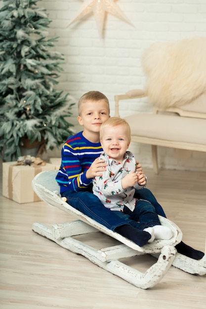 Weihnachten ist schon da. Zwei Brüder, die mit Weihnachtsgeschenkbox rodeln. Kleiner netter Junge erhielt Feriengeschenke. Kindergriff-Geschenkbox beim Rodeln. Weihnachten feiern. Winteraktivität