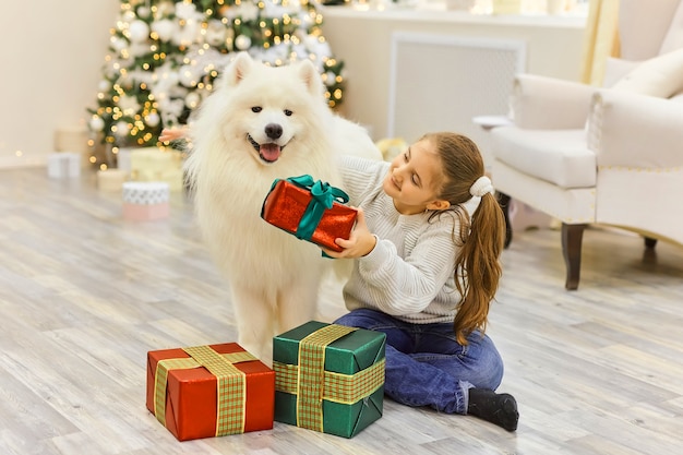 Weihnachten Kind Mädchen Umarmung Hund Samojede. Weihnachts-, Winter- und Menschenkonzept.