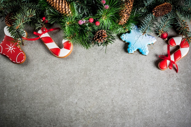 Weihnachten mit Tannenbaumast, selbst gemachten bunten Lebkuchenplätzchen, Kiefernkegeln und Dekorationen auf grauer Steintabelle. Draufsicht, Exemplar