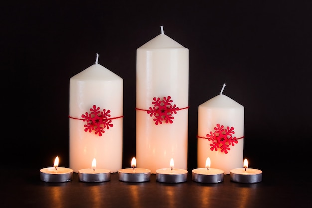 Weihnachten, Neujahrsgrußkarte mit drei großen weißen Kerzen, roten Schneeflocken und vielen kleinen brennenden Kerzen auf schwarzem Hintergrund.