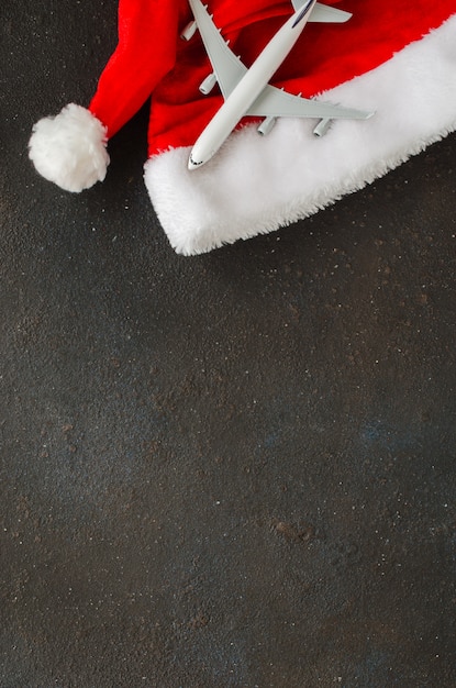 Weihnachten oder Neujahr Reisekonzept. Spielzeugflugzeug und Sankt-Hut auf dunklem Beton.