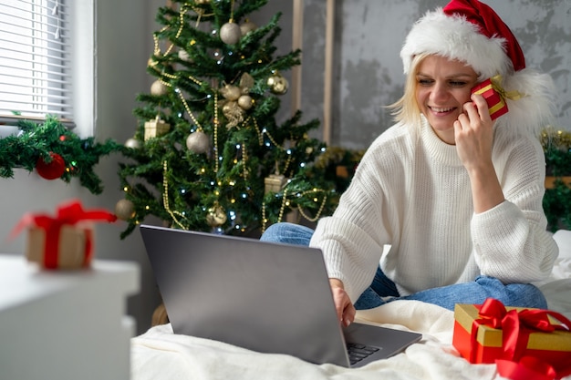 Weihnachten Online-Shopping. Mädchen Käufer macht Bestellung auf Laptop. Frau kaufen Geschenke, bereiten sich auf Weihnachten vor, zwischen Geschenkboxen und Paketen. Verkauf von Winterferien.
