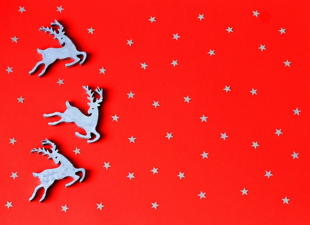 Foto weihnachten spielt hölzerne rotwild auf rotem papierhintergrund mit dekorativen sternen.