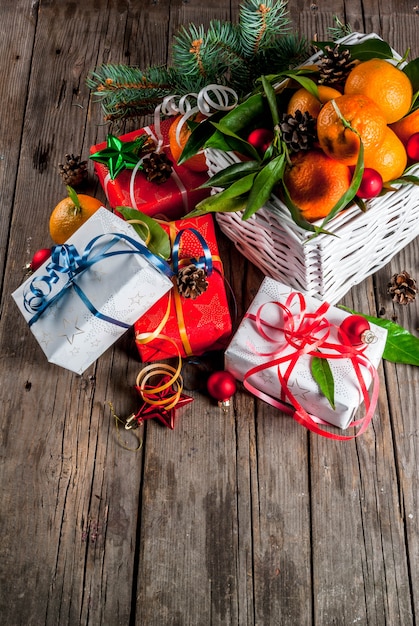 Weihnachten und Neujahr Konzept. Frische Tangerinen mit Grün verlässt in einem weißen Korb, in einer Weihnachtsdekoration und in Geschenkboxen, auf altem rustikalem Holztisch, Draufsicht