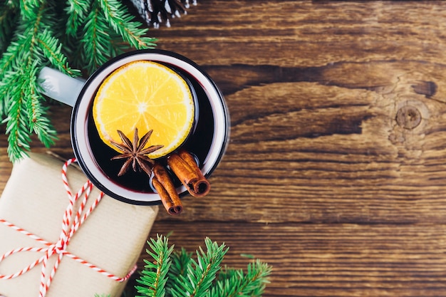 Weihnachten und Neujahr trinken heißen Wein, Glühwein, Punsch oder Tee auf einem hölzernen Hintergrund neben einem grünen Weihnachtsbaum und einer Schachtel mit einem Geschenk. Platz für Text.