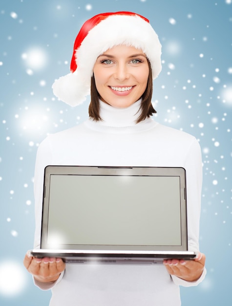 Weihnachten, Weihnachten, Elektronik, Gadget-Konzept - lächelnde Frau in Weihnachtsmann-Helfermütze mit Laptop-Computer mit leerem Bildschirm