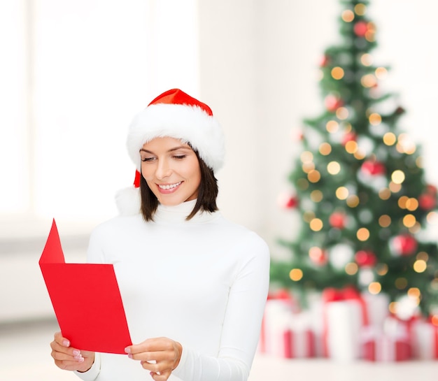 Weihnachten, Weihnachten, Leute, Werbung, Verkaufskonzept - glückliche Frau in Weihnachtsmann-Helfermütze mit leerer roter Postkarte