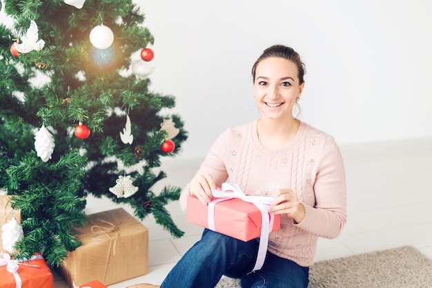Weihnachten, Weihnachten, Winter, Glückskonzept - Mädchen öffnet ein Geschenk vor dem Hintergrund des Weihnachtsbaums. Glückliche junge Frau, die Weihnachten feiert