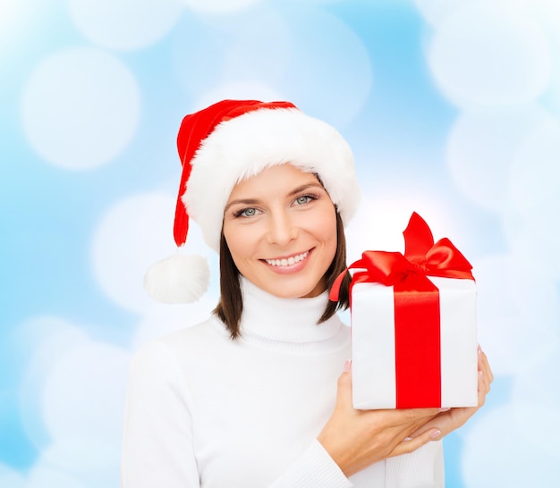 weihnachten, winter, glück, feiertage und menschenkonzept - lächelnde frau in weihnachtsmannmütze mit geschenkbox über blaulichthintergrund