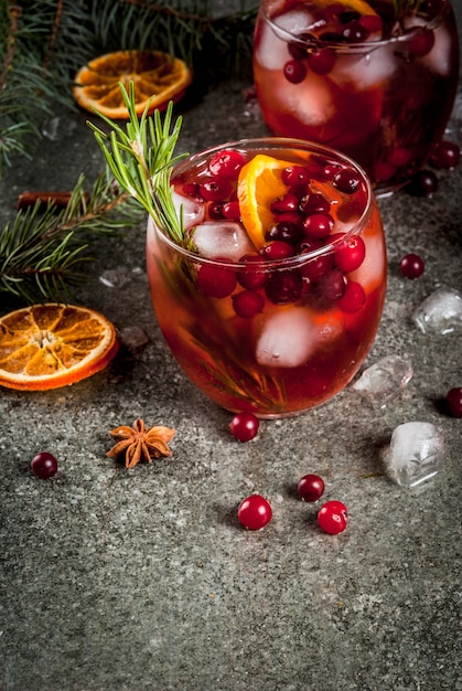 Weihnachten Wintergetränke. Kaltes Cocktail mit Moosbeeren, Orange, Rosmarin, mit Gewürzen (Zimt, Anis) und Eis, auf einer dunklen Steintabelle, copyspace