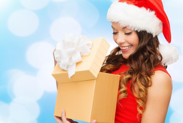 weihnachts-, feiertags-, feier- und menschenkonzept - lächelnde frau im roten kleid mit kleiner geschenkbox über blaulichthintergrund