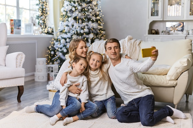 Weihnachts-, Feiertags-, Technologie- und Menschenkonzept - glückliche Familie, die im Wohnzimmer sitzt und zu Hause ein Selfie-Foto mit dem Smartphone macht