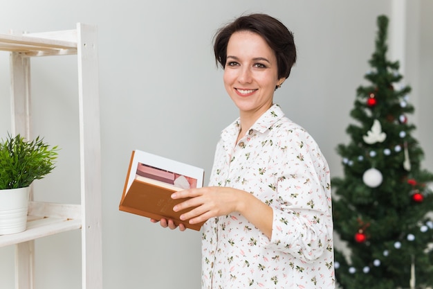 Weihnachts-, Feiertags- und Personenkonzept - glückliche junge Frau, die Buch zu Hause liest.