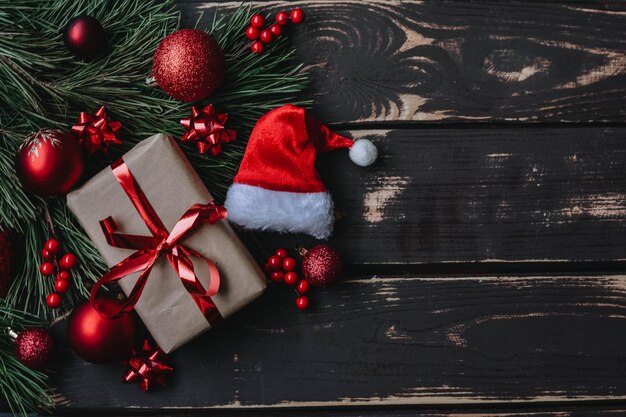 Weihnachts-Flatlay-Geschenkbox, rotes Weihnachtsbaumspielzeug, Weihnachtsmütze und Fichtenzweig auf Holzbackgro