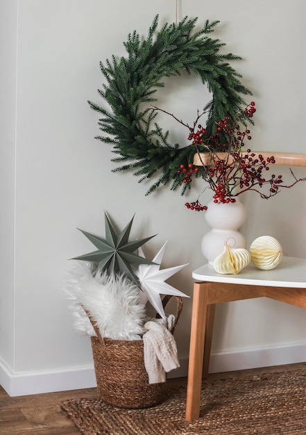 Foto weihnachts-interieurkomposition ein korb mit gefiederten skandinavischen sternen ein weihnachtskränz an der wand eine vase mit cranberry-zweigen auf einem stuhl skandinavischer stil