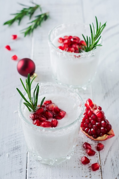 Weihnachts-Kokosnuss-Punsch mit Granatapfelkernen und Rosmarinzweigen auf heller Oberfläche