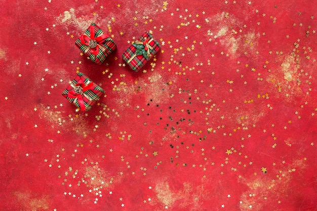 Weihnachts-Neujahrs-Geschenkboxen auf festlichem rotem und goldenem Hintergrund mit goldenem, glitzerndem, sternförmigem Konfetti Draufsicht aus nächster Nähe