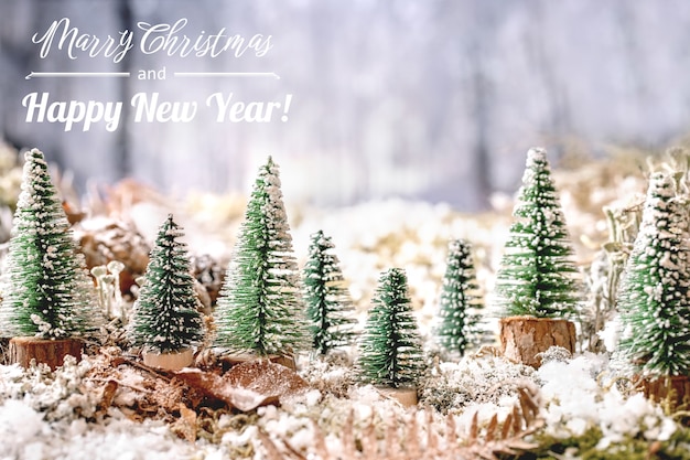 Weihnachts- oder Neujahrsgrußkarte mit einer Gruppe dekorativer Weihnachtsbäume auf schneebedecktem Moos mit Winterwald im Hintergrund. Weihnachtsferien Atmosphäre. Grußtext enthalten