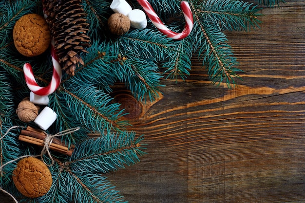 Weihnachts- oder neujahrshintergrund mit keksen, gewürzen, zimt, nüssen und tannenzweig auf dunklem holzhintergrund.