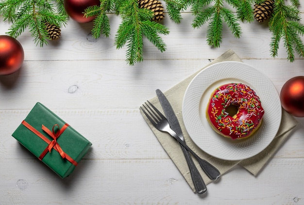 Weihnachts- oder Neujahrshintergrund mit Weihnachtsbaum, Geschenk, Donut auf einem Teller auf einer weißen Tafel