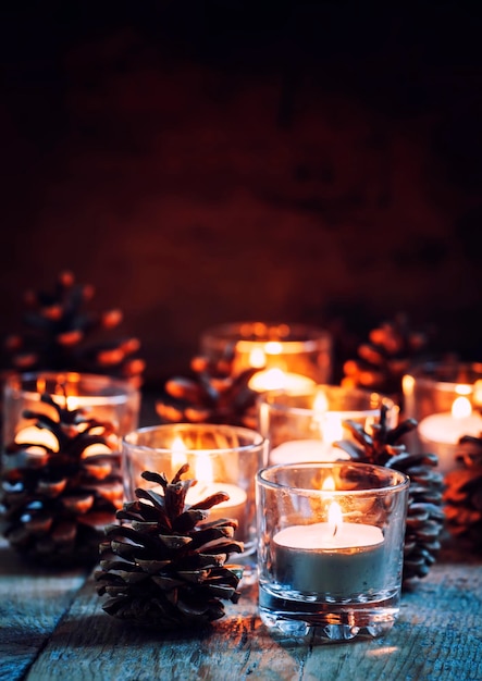 Weihnachts- oder Neujahrskomposition mit brennenden Kerzen in kleinen Glaskerzenhaltern und Tannenzapfen Vintage Holzhintergrund festlicher Abend selektiver Fokus