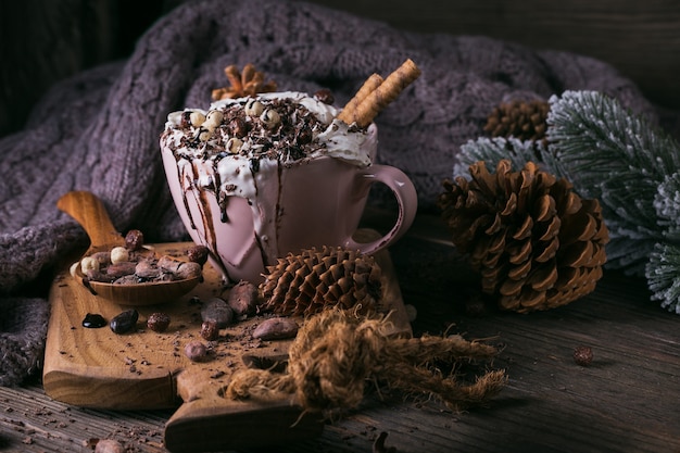 Weihnachts- oder Neujahrskomposition mit heißer Schokolade oder Kakaogetränk mit Schlagsahne, serviert mit gehackter Schokolade und Kakaobohnen auf rustikalem Holzteller.