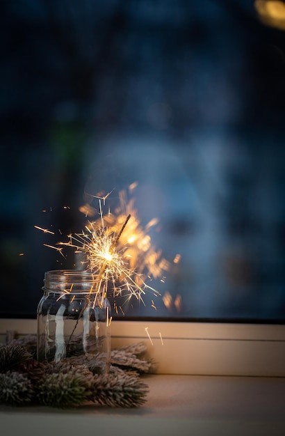 Weihnachts- oder Neujahrsparty Wunderkerze in einem Glas vor dem Fenster auf dunklem Hintergrund Weihnachtsdekoration