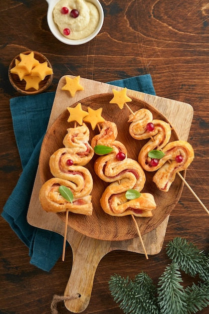 Weihnachts- oder Neujahrsvorspeise Weihnachtsbaumform Blätterteigbrötchen mit Käse und Schinken Gruppe von Weihnachtsbaumformen auf Holzbrett Festliche Idee für Weihnachts- oder Neujahrsessen Draufsicht