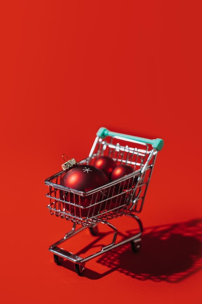 Weihnachts-Shopping-Wagen mit roten Xmas-Ornamenten, Kugeln auf rotem Hintergrund, minimaler Weihnachten-Shopping, Verkaufs-Web-Banner-Kopierraum-Konzept