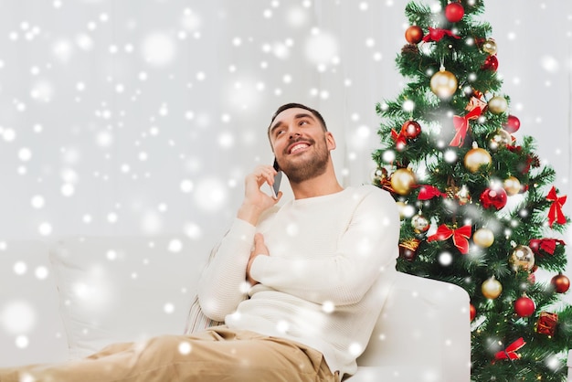 weihnachts-, technologie-, menschen- und feiertagskonzept - lächelnder mann, der zu hause auf dem smartphone anruft