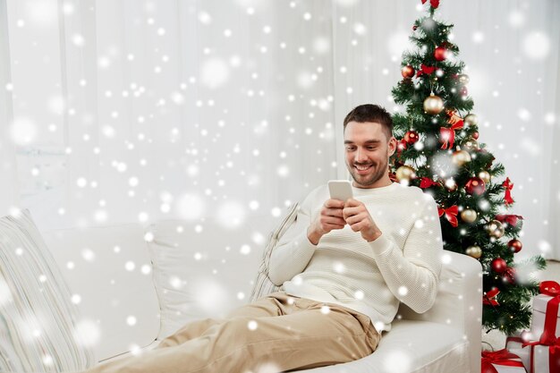 weihnachts-, technologie-, personen- und feiertagskonzept - lächelnder mann mit smartphone-sms-nachricht zu hause