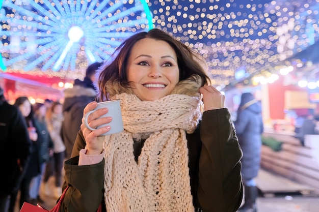 Weihnachts- und Neujahrsfeiertage, glückliche reife schöne Frau mit Einkaufstüten und Tasse heißem Getränk am Weihnachtsmarkt